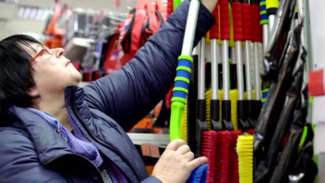 Eine-reife-Frau-wählt-eine-Bürste-mit-Schaber-im-Supermarkt.