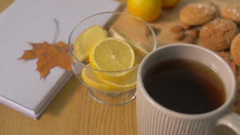 Buch,-Zitrone,-Tasse-Tee,-Nüsse-und-Gebäck-auf-Tisch