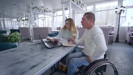 education-courses-for-disabled,-Smart-aching-student-mature-men-in-wheelchair-with-tutor-female-during-home-education-using-modern-computer-technology