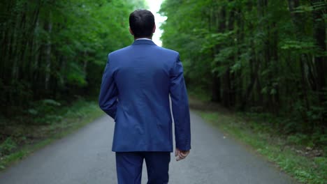 handsome-young-businessman-walking-along-the-road-in-forest,-view-back