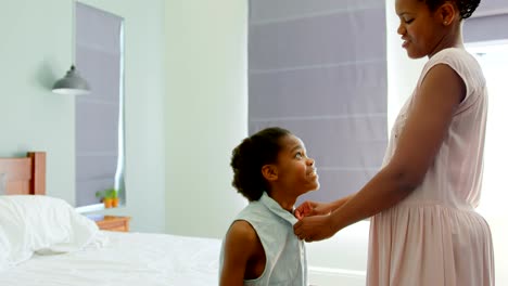 Side-view-of-mid-adult-black-mother-helping-her-daughter-in-wearing-dress-in-a-comfortable-home-4k