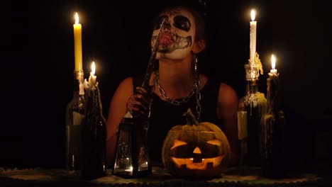 Halloween-witch-licks-knife-blade-in-chains-with-skull-makeup-magic-pumpkin-and-candles