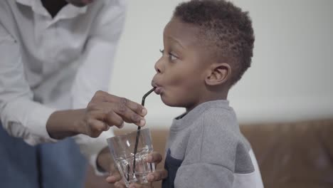 Caring-mother-helping-little-african-american-boy-to-drink-water