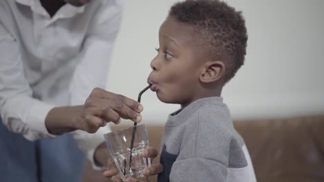 Betreuende-Mutter-hilft-kleinen-afrikanischen-Amerikanischen-Jungen,-Wasser-zu-trinken