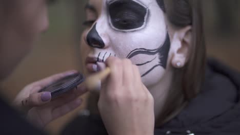 Primer-plano-de-una-chica-caucásica-pintando-maquillaje-de-Halloween-en-la-cara-de-su-amiga.