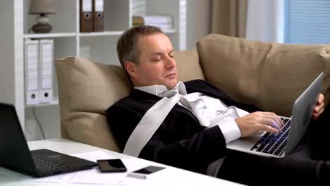 Tired-businessman-working-with-laptop-and-falls-asleep-on-the-sofa-at-the-office