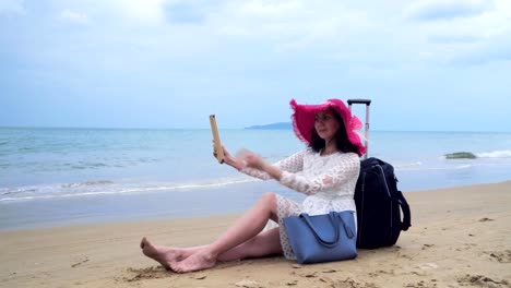 Girl-seats-on-the-beach-with-her-bagage-and-tablet-computer