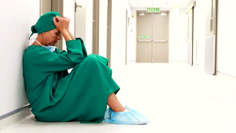 Tensed-female-surgeon-sitting-in-corridor