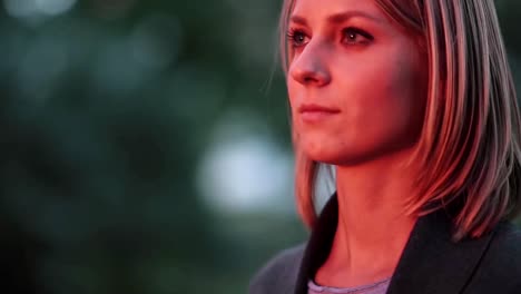 Attractive-young-woman-standing-at-park-in-the-rays-of-the-setting-sun-and-looking-into-the-distance.-Close-up