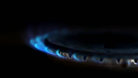 Close-up-of-gas-stove-blue-flame-lit-in-a-dark-kitchen