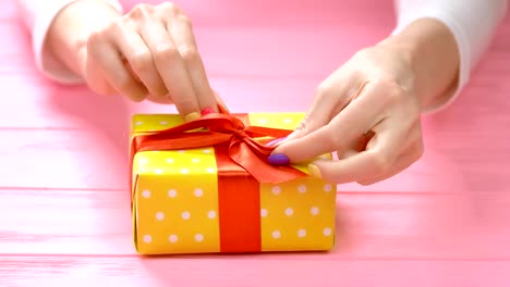 Manicured-hands-ties-ribbon-on-gift-box.