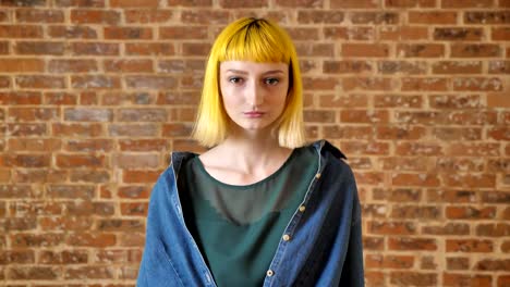 Young-beautiful-woman-with-yellow-hair-looking-at-camera-and-standing-near-brick-wall-background,-unusual-people