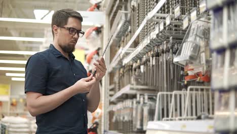 Male-shopper-is-taking-big-metal-drill-bit-from-racks-in-a-shop-for-builders