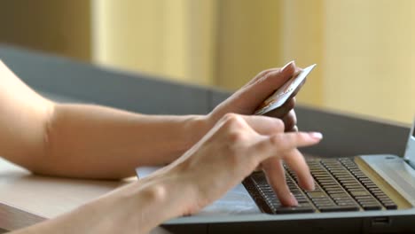 Close-up-woman's-hands-holding-a-credit-card-and-using-computer-keyboard-for-online-shopping