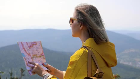 Wanderer-in-einem-gelben-Regenmantel,-Blick-auf-Karte-von-Berg.-Frau-mit-Karte-in-Bergen-FullHD