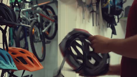 A-young-Caucasian-man-stands-near-a-stand-in-a-bicycle-store-in-the-head-protection-department.-Choosing-a-bicycle-helmet-in-a-small-store