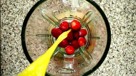 O-Saft-fließt-in-einen-Mixer-Schüssel-auf-Erdbeere.-Slow-Motion.	Dreharbeiten-in-der-Küche.-Ansicht-von-oben.