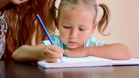 Kleine-süße-Mädchen-sitzt-im-Klassenzimmer-und-Studien-mit-Lehrer-im-Heft