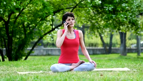 Chica-está-hablando-en-un-teléfono-móvil-durante-yoga-ejercicio-entrenamiento