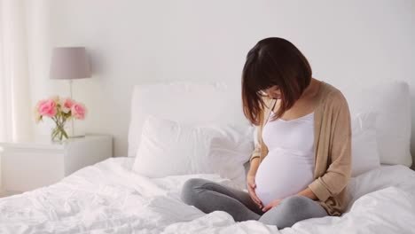 mujer-asiática-Embarazada-feliz-sentado-en-la-cama-en-casa