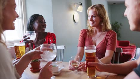 Five-young-adult-friends-sitting-with-drinks-at-a-table-in-a-pub-talking-and-laughing,-close-up,-low-angle