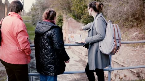 Joven-hermosa-Europeo-femenino-guía-dando-un-paseo-a-dos-mujeres-mayores-alrededor-de-antiguas-ruinas-en-Ostia,-Italia.