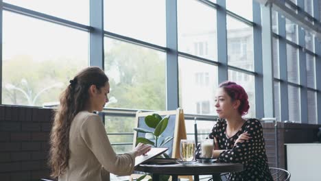 Woman-drawing-sketch-and-talking-with-friend-at-cafe