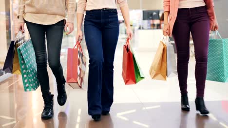 Low-shot-of-ladies'-legs-walking-in-shopping-center-with-paper-bags-enjoying-buying-clothes-and-presents.-Youth-lifestyle,-friendship-and-consumerism-concept.