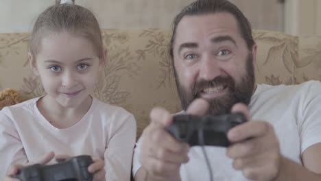 Small-daughter-with-her-funny-father-playing-video-games-on-tv-with-great-emotions-in-cozy-living-room.