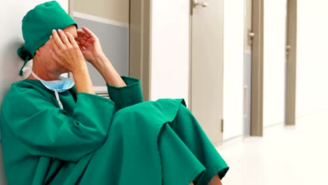 Tensed-female-surgeon-sitting-in-corridor