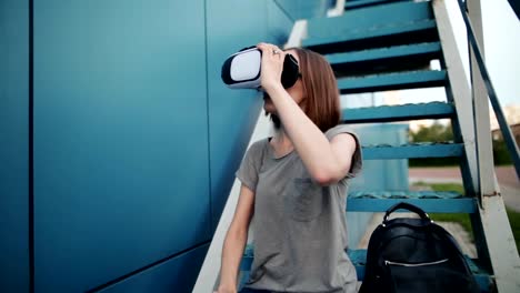 Zukunft-ist-jetzt.-Schöne-junge-Frau-auf-einer-Treppe-Rollenspiel-in-Vr-Brille.-Kaukasische-Mädchen-berühren-etwas-mit-modernen-virtual-Reality-Brille-auf-blauem-Grund.