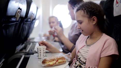 Young-woman-sits-in-chair-near-illuminator-of-airplane-and-eats-meal-for-passenger