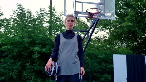 Alguien-tirar-a-jugadora-baloncesto,-aro-bola-cogida-mujer-y-mirando-a-cámara,-en-el-parque,-en-fondo