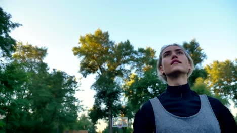 Beautiful-female-basketball-player-throwing-ball,-playing-in-park-with-blue-sky-above,-low-angle