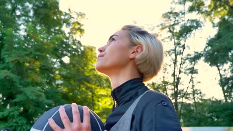 Beautiful-blonde-woman-preparing-to-throw-basketball,-standing-in-park-and-playing,-lens-flare