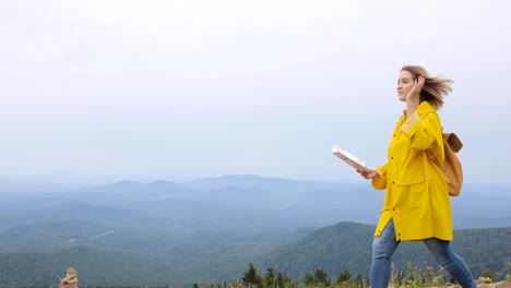 Joven-mujer-trekking-impermeable-amarillo-de-im-con-una-mochila-en-montañas-con-mapa-de-papel-en-las-manos