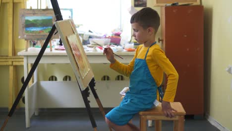 Pensive-boy-painting-with-oil-paints-during-class