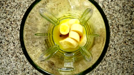 Pedazos-de-manzanas-caen-en-un-recipiente-de-la-licuadora-en-trozos-de-plátanos.-Cámara-lenta.	Disparos-en-cocina.-Vista-superior.