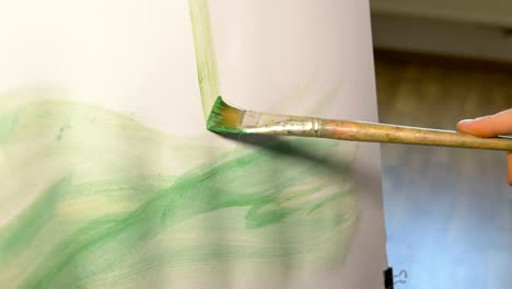 Artist-makes-a-vertical-line-of-green-paint-using-a-brush-for-painting-on-canvas.-Leisure-of-creative-and-unusual-people.