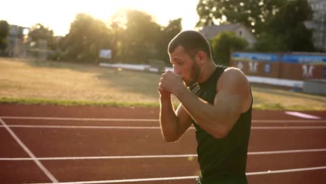 Slow-motion-of-concentrated-man-boxer-doing-boxing-exercise,-warming-up-while-standing-on-stadium-outdoors-in-summer-sun-rays.-Side-view