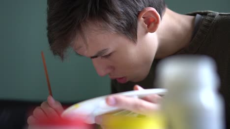 Student-boy-with-paintbrushe-and-palette-painting-at-studio