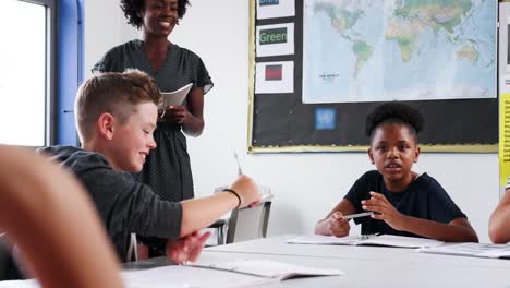 Mujer-secundaria-Tutor-docente-grupo-de-estudiantes-que-trabajan-alrededor-de-la-mesa-en-el-salón-de-clases