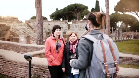 Joven-hermosa-chica-Europea-tomando-una-foto-de-dos-mujeres-mayores-cerca-de-antiguas-ruinas-históricas-en-Ostia,-Italia-de-vacaciones.