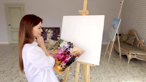 A-young-sexy-girl-in-a-white-shirt-draws-on-canvas-in-the-studio-for-drawing.Art