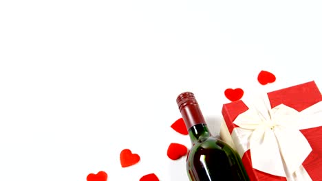 Wine-bottle,-gift-box-and-scattered-red-hearts-on-white-surface-4k