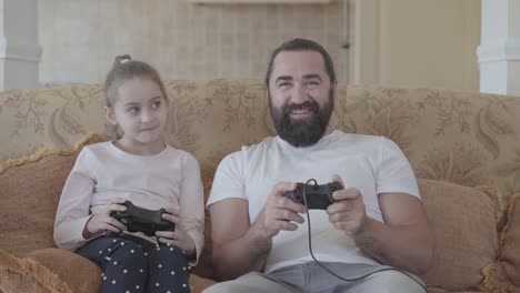 Pequeña-hija-con-su-divertido-padre-jugando-videojuegos-en-la-televisión-con-grandes-emociones-en-la-acogedora-sala-de-estar.