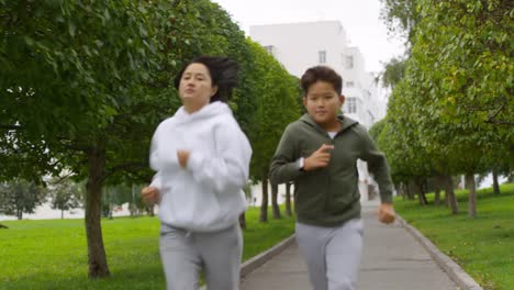 Asian-Mother-and-Son-Running-along-Green-Alley-with-Trees