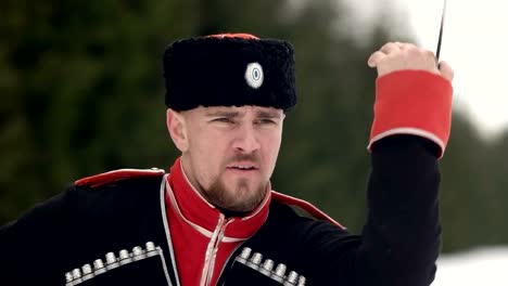 A-young-man-in-Cossack-clothes-swinging-a-sword-in-a-winter-landscape-in-the-snow.