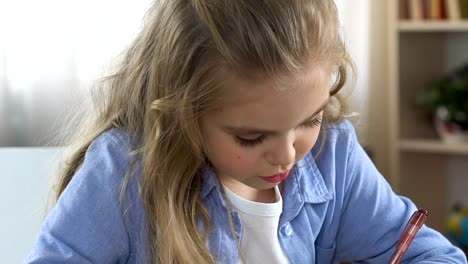 Concentrated-school-girl-doing-homework-exercise-in-notebook,-home-schooling