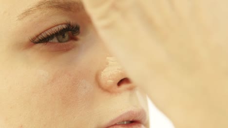 Mujer-joven-de-rostro-durante-la-aplicación-de-crema-de-base-en-piel-en-estudio-de-maquillaje.-Profesional-visagiste-haciendo-cara-de-mujer-de-maquillaje-antes-de-foto-o-video-disparos-en-vestidor